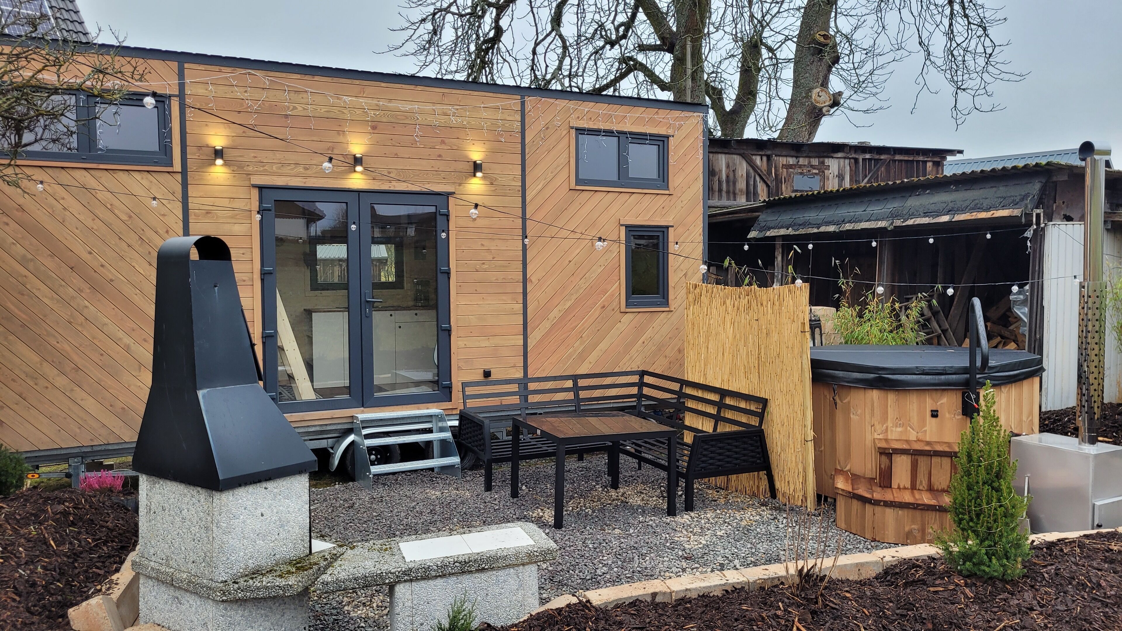 Een modern terras buiten met een barbecue, zithoek en lichtjes.