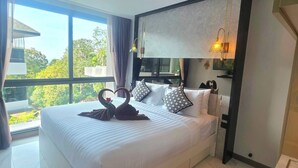 Una camera d'albergo con un letto grande, vista sugli alberi dalla finestra e un lampadario moderno sopra il letto.