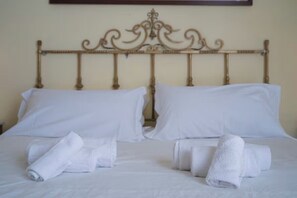 A neatly made bed with white linens and rolled towels, a classic metal headboard, and a simple wall-mounted light fixture. - To complete (Catania)