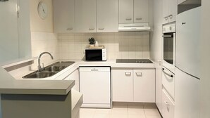 Una cucina moderna con mobili bianchi, forno a microonde integrato, lavastoviglie e frigorifero.