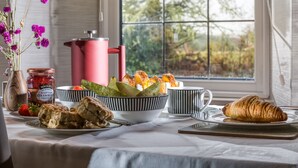 Colazione con croissant, scones, fragole e barattolo di marmellata su un tavolo vicino a una finestra che si affaccia sul verde.
