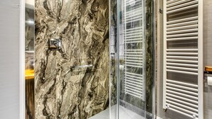 Un bagno moderno con parete in marmo, cabina doccia in vetro e porta asciugamani bianco.