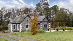 Una casa in pietra con tetto grigio, un portico in legno e un vialetto sterrato.