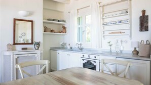 A kitchen with white cabinetry, a wooden table, and a window with curtains. - Cycladic Cottage with sea access in a hideaway of rare character (Andros)