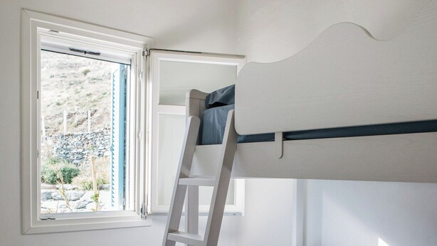 A bunk bed with a ladder, a window with a view of a garden, and a stone-patterned floor. - Cycladic Cottage with sea access in a hideaway of rare character (Andros)