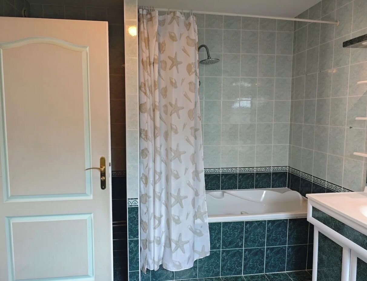 Une salle de bain avec une baignoire, un rideau de douche orné de motifs d’étoiles de mer et une porte dotée d’une poignée en laiton.