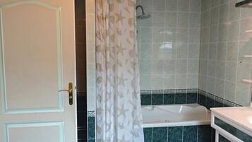 Une salle de bain avec une baignoire, un rideau de douche orné de motifs d’étoiles de mer et une porte dotée d’une poignée en laiton.