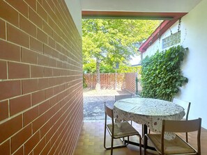 Eine Terrasse mit einer Ziegelmauer, einem runden Tisch mit Stühlen und Blick auf einen Garten mit Bäumen und einem Zaun.