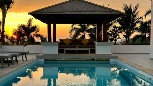 Una piscina con un pabellón, palmeras y vistas al atardecer.