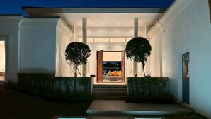 Una casa moderna con una entrada bien iluminada, dos árboles y un camino que lleva a la puerta.