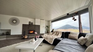 Una sala de estar moderna con chimenea, un ventanal con vistas a la montaña, un sofá y una mesa de centro.
