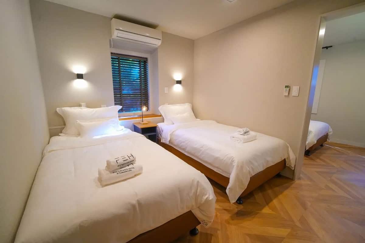 A hotel room with two beds, a nightstand, and an air conditioning unit.