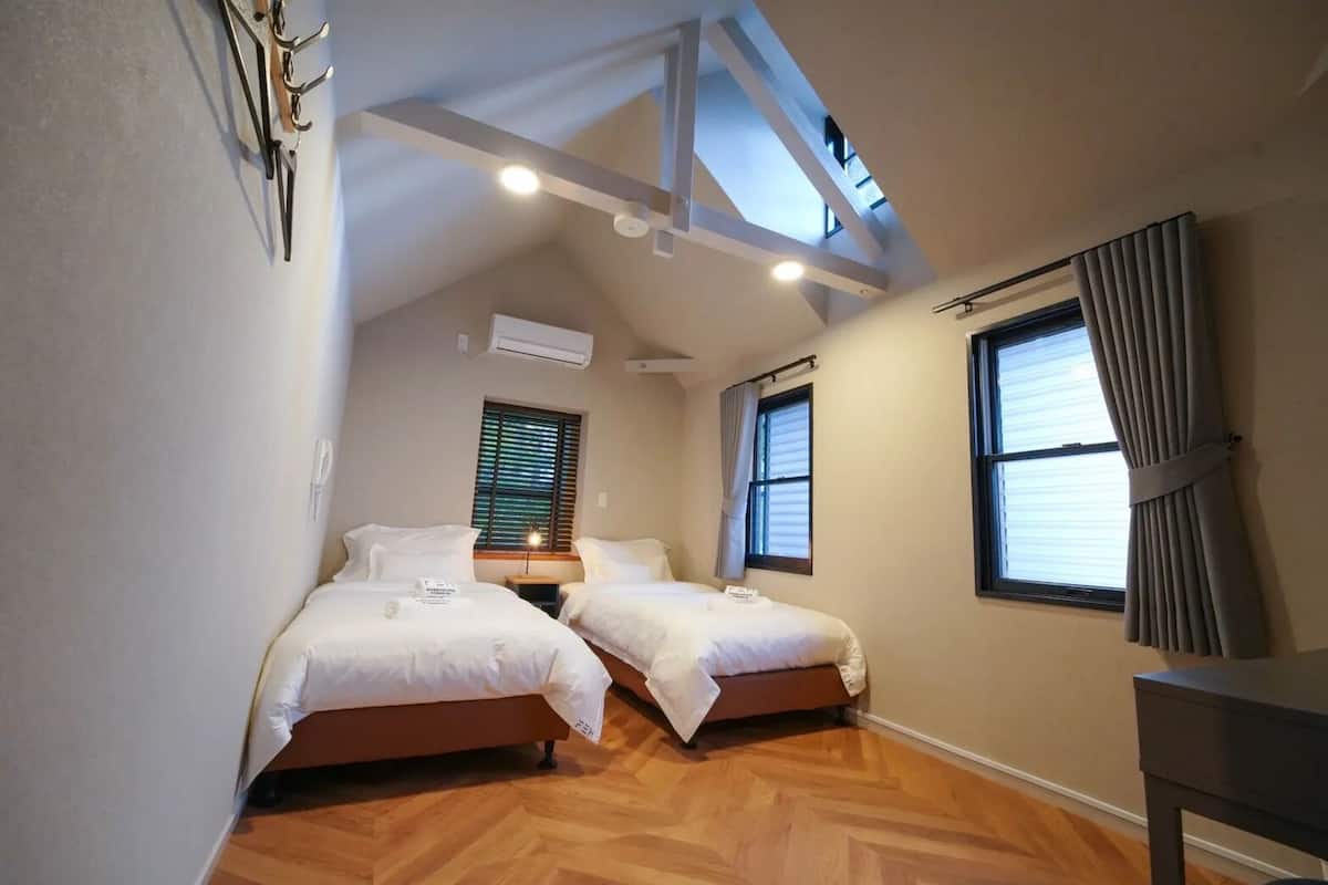 A bedroom with two beds, wooden flooring, a skylight, and a window with curtains.