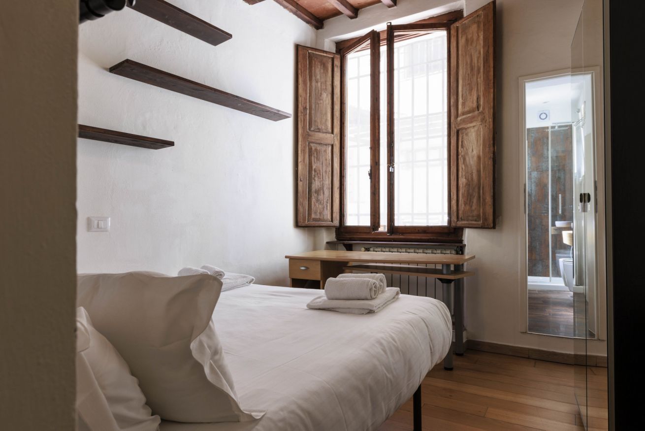 Een slaapkamer met een bed, een raam met houten luiken, een radiator en een deur naar een balkon.