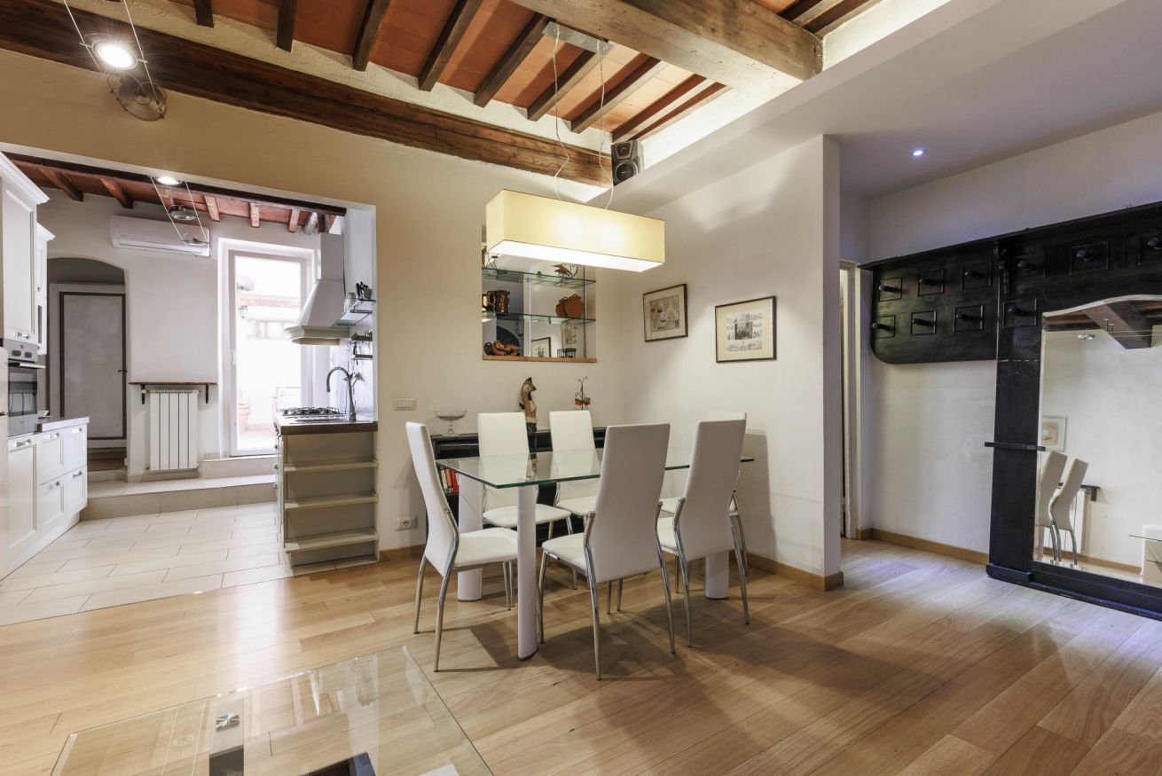 Une cuisine moderne avec des meubles blancs, une table à manger en verre et un plafond en bois.