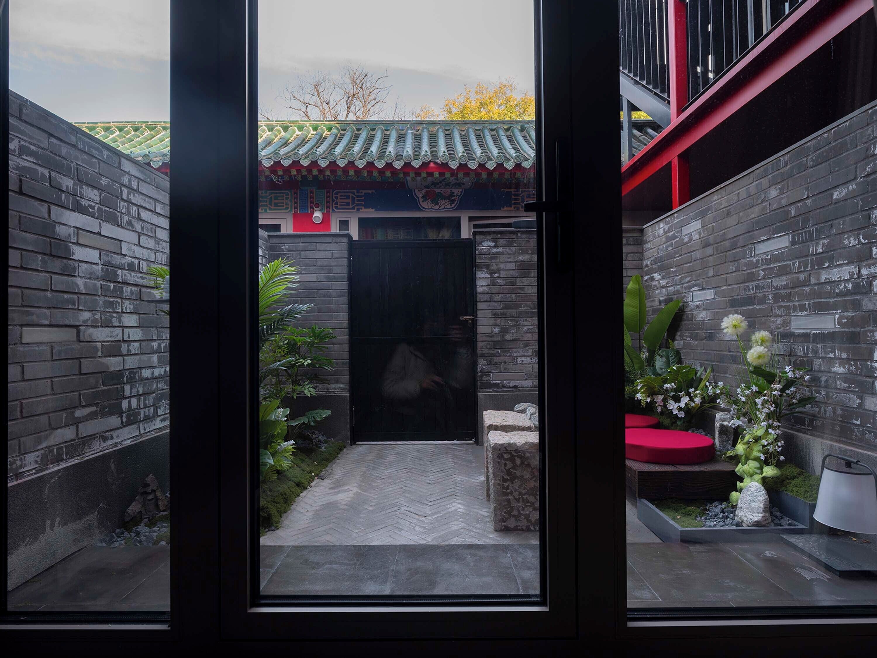 A narrow courtyard with a traditional tiled roof, a stone pathway, and a red bench.