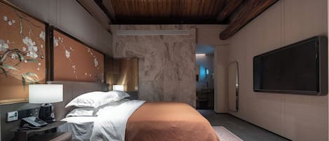 Una habitación de hotel moderna con una cama, un escritorio, una silla, un televisor y un baño visible a través de una puerta abierta.