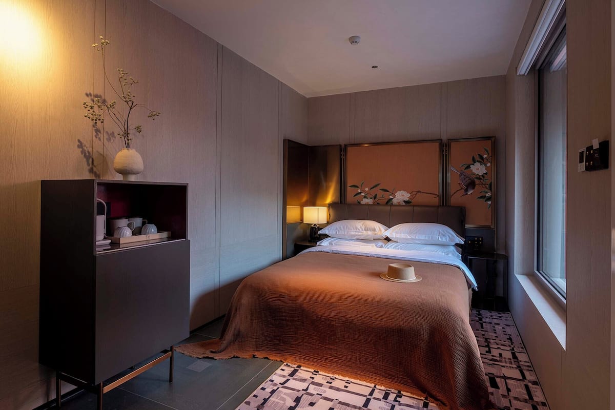 Una habitación de hotel moderna con una cama, mesita de noche, lámpara y un adorno en la pared.