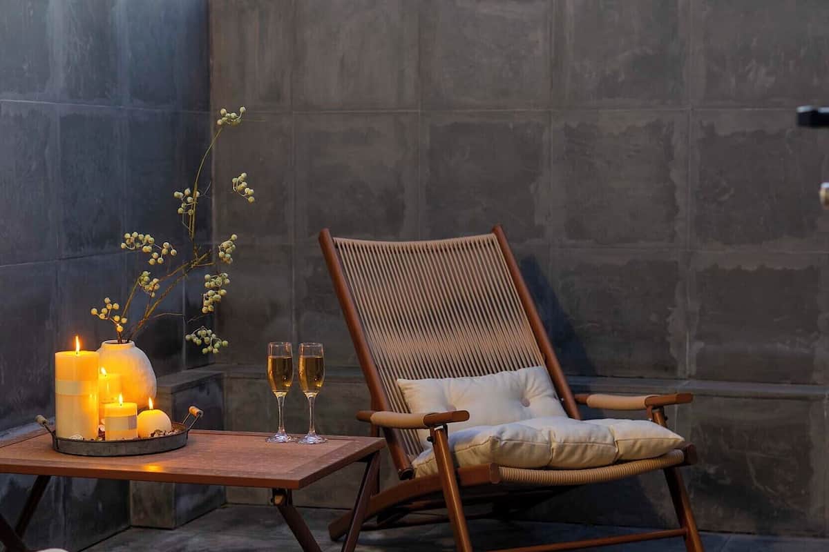 Un rincón al aire libre acogedor con una silla y mesa de madera, velas y un libro.
