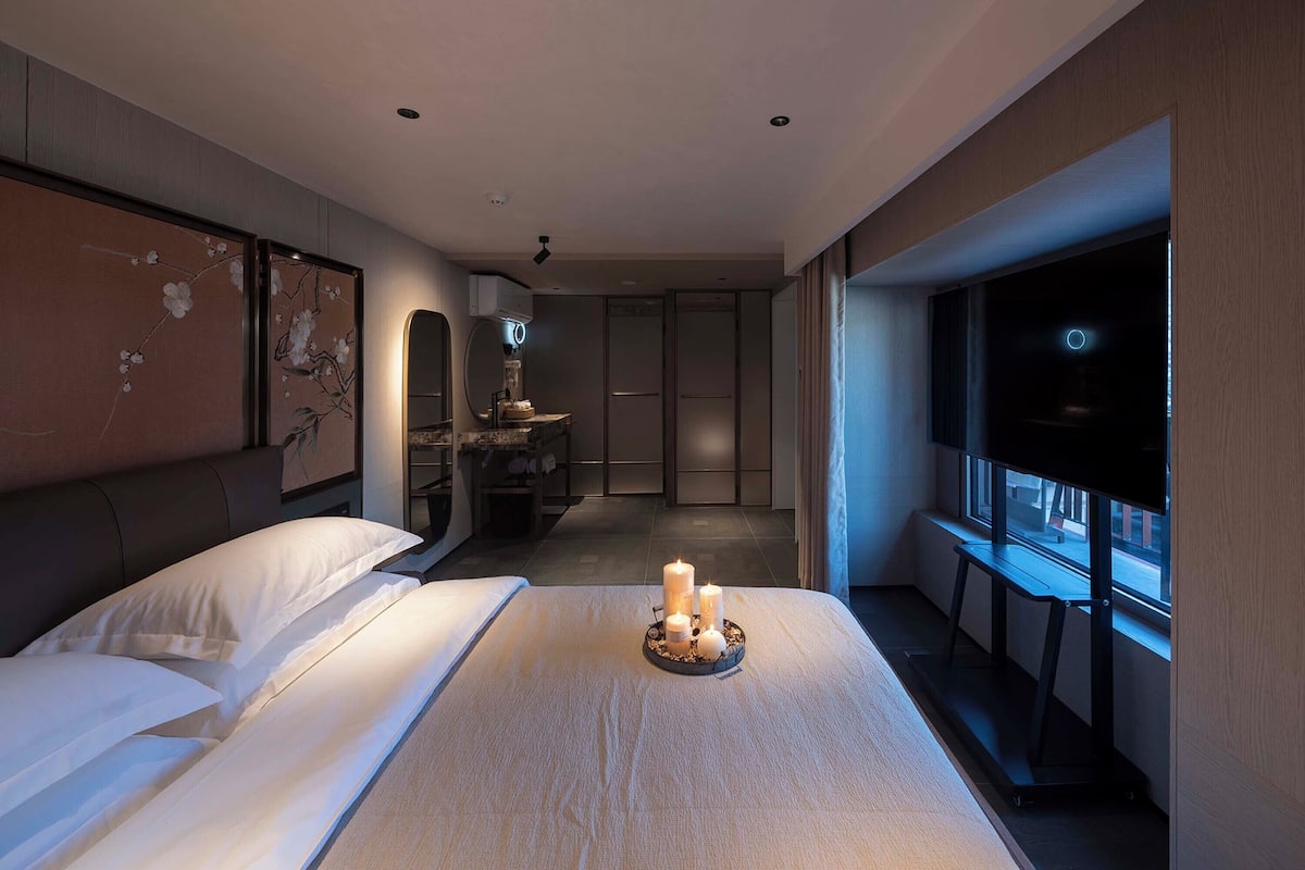 Una habitación de hotel moderna con una cama grande, un tocador con espejo, una mesita y una ventana con vistas.