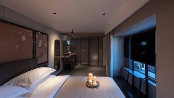 A modern hotel room with a large bed, a vanity with a mirror, a small table, and a window with a view.