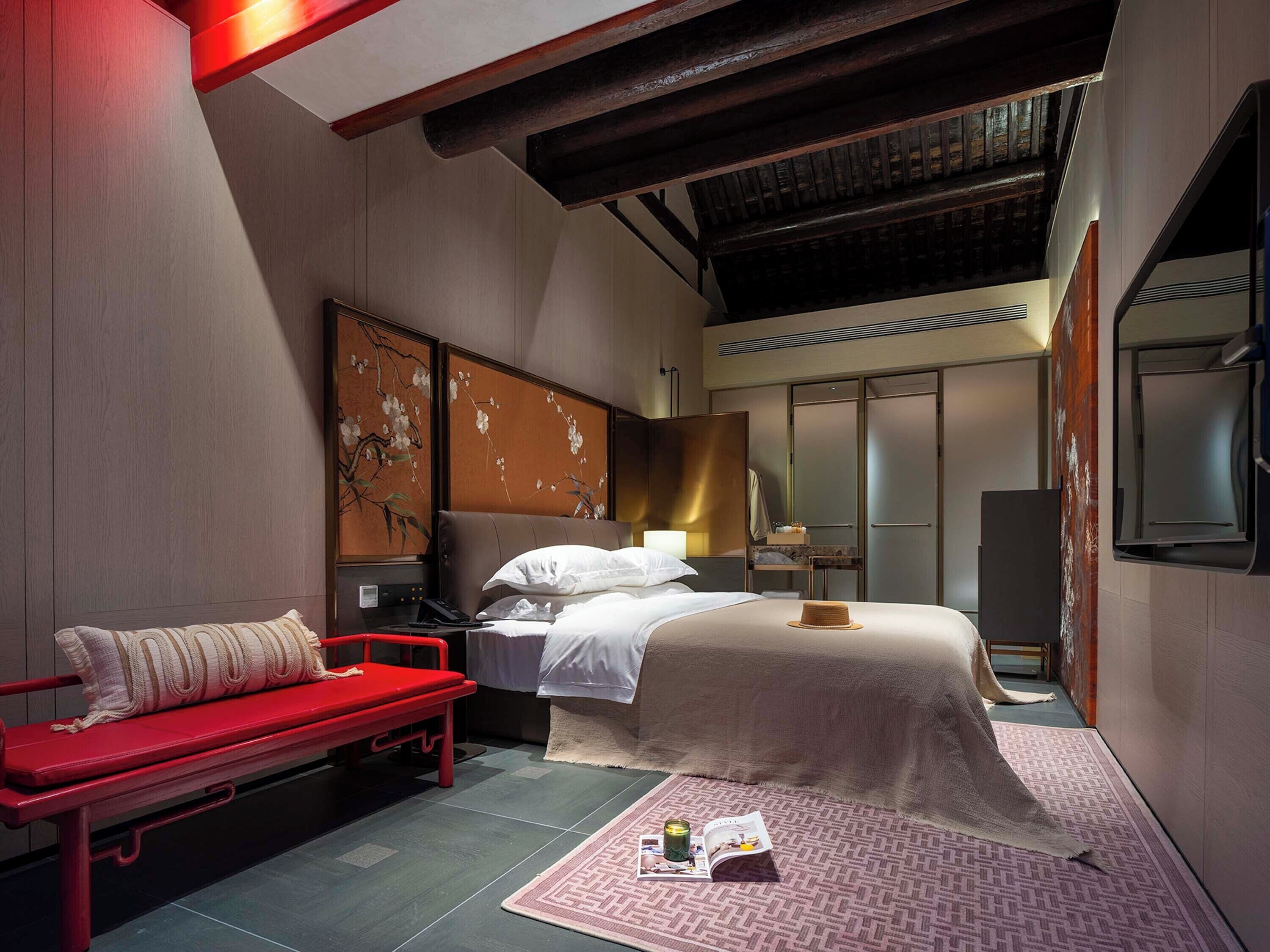 Une chambre d’hôtel moderne avec un lit, un banc rouge, un bureau et un grand miroir.