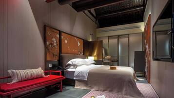 Une chambre d’hôtel moderne avec un lit, un banc rouge, un bureau et un grand miroir.