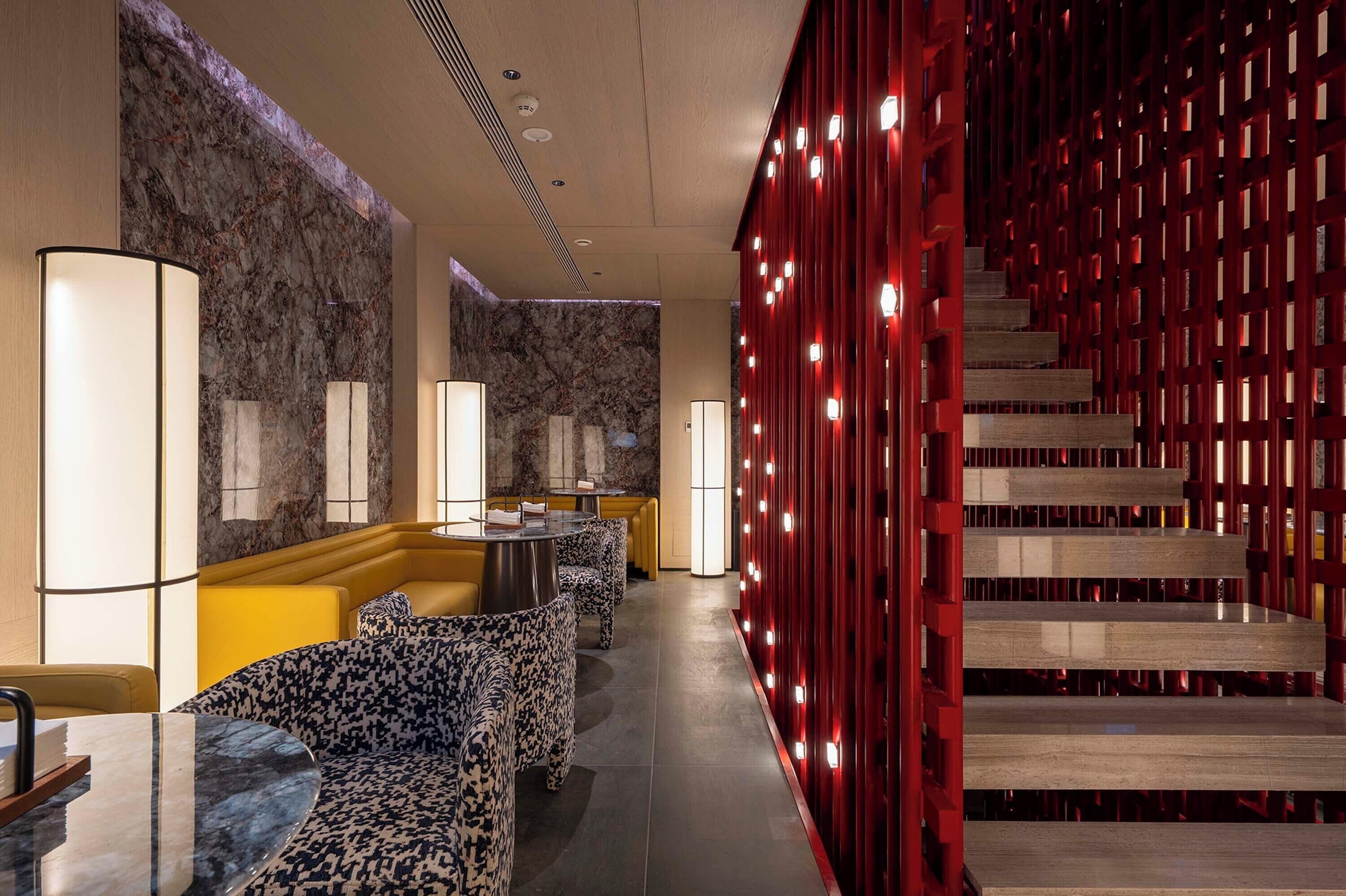 A modern hotel lobby with marble walls, a yellow seating area, and a red decorative wall with lights.
