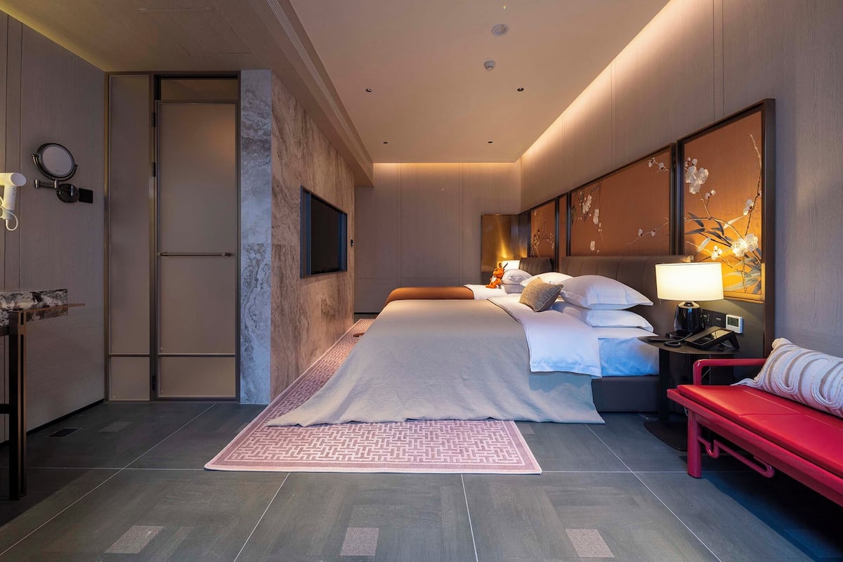 Una habitación de hotel moderna con una cama grande, un escritorio y un banco rojo.