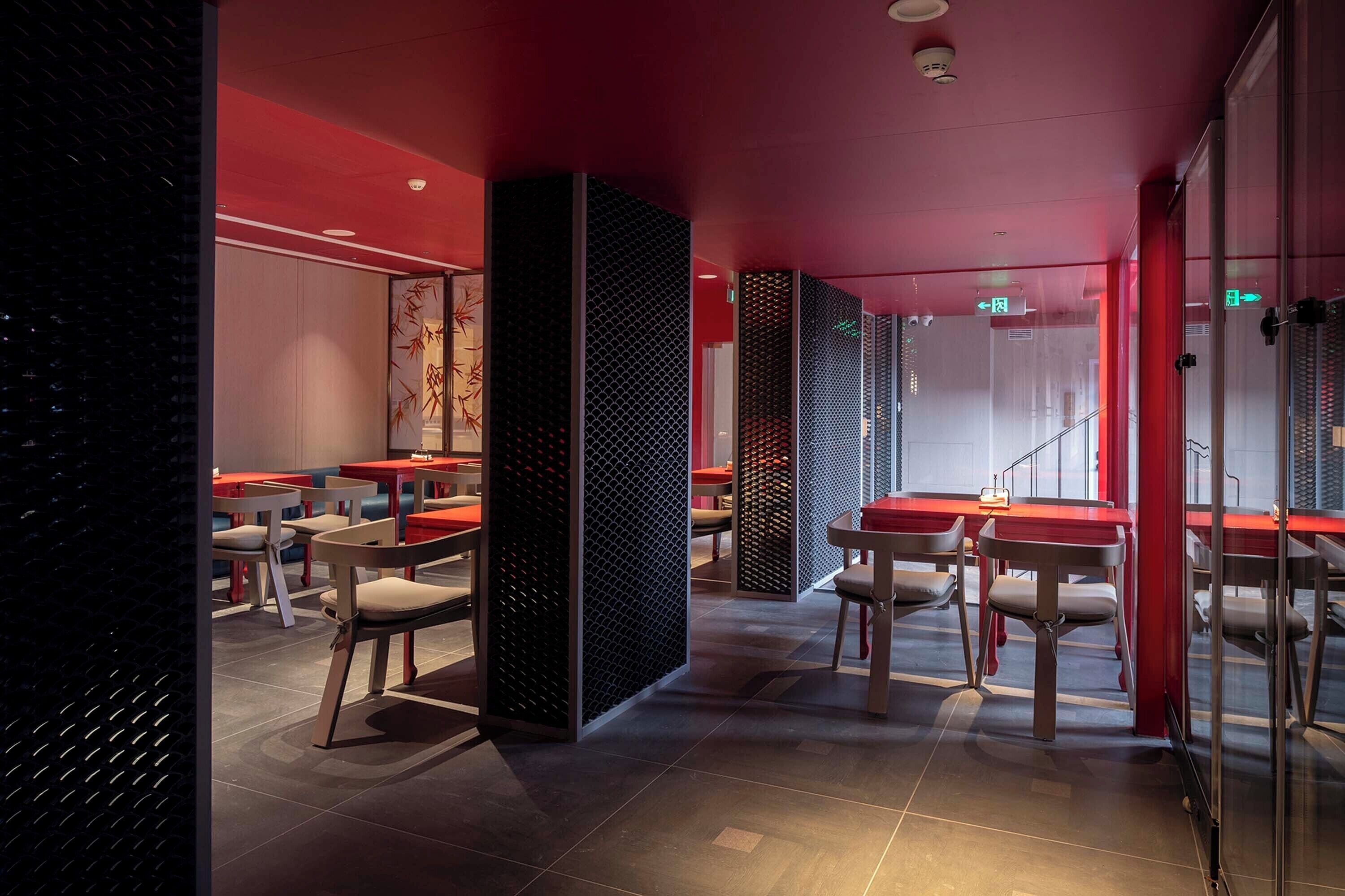 A modern restaurant interior with red accents, glass partitions, and contemporary furniture.