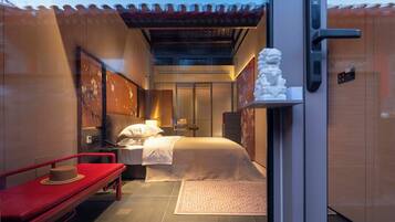 A hotel room with a bed, a red bench, a decorative statue, and a traditional-style ceiling.