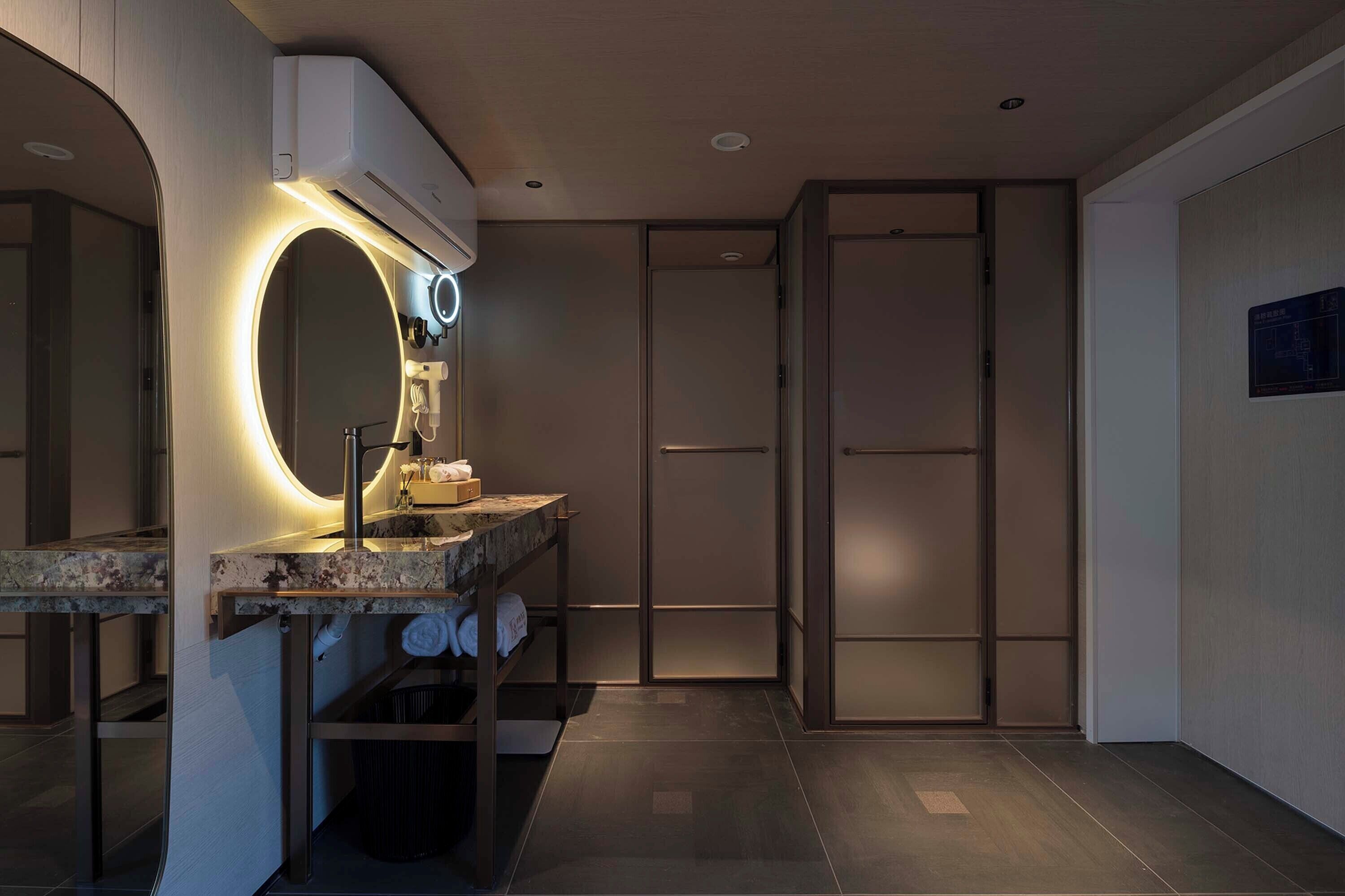 A modern bathroom with a vanity, a large mirror with built-in lighting, a towel rack, and a toilet.