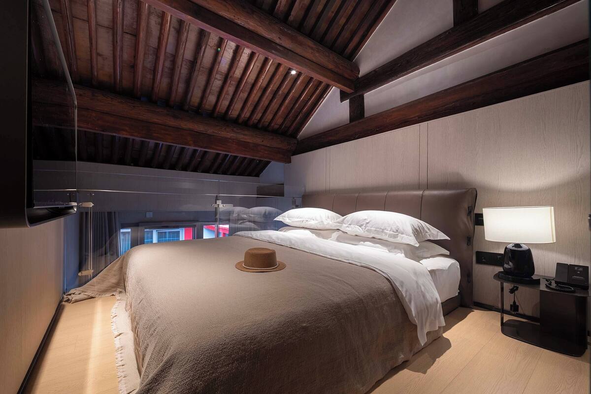 Un dormitorio con una cama grande, una mesita de noche, una lámpara y vistas al exterior.