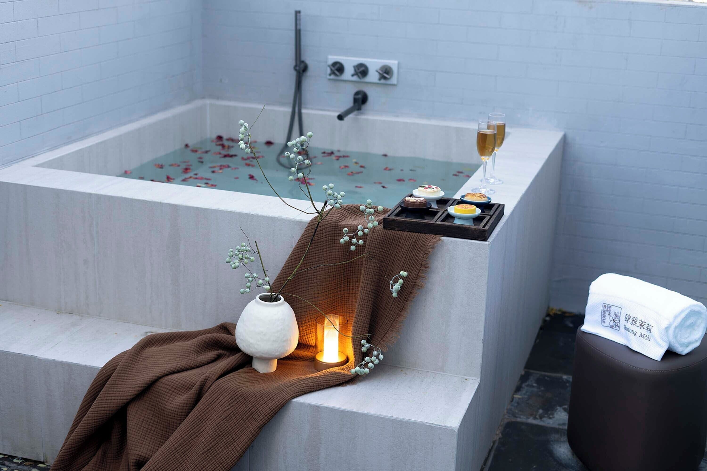 Un baño moderno con bañera, una toalla, una vela y una bandeja con comida y bebidas.