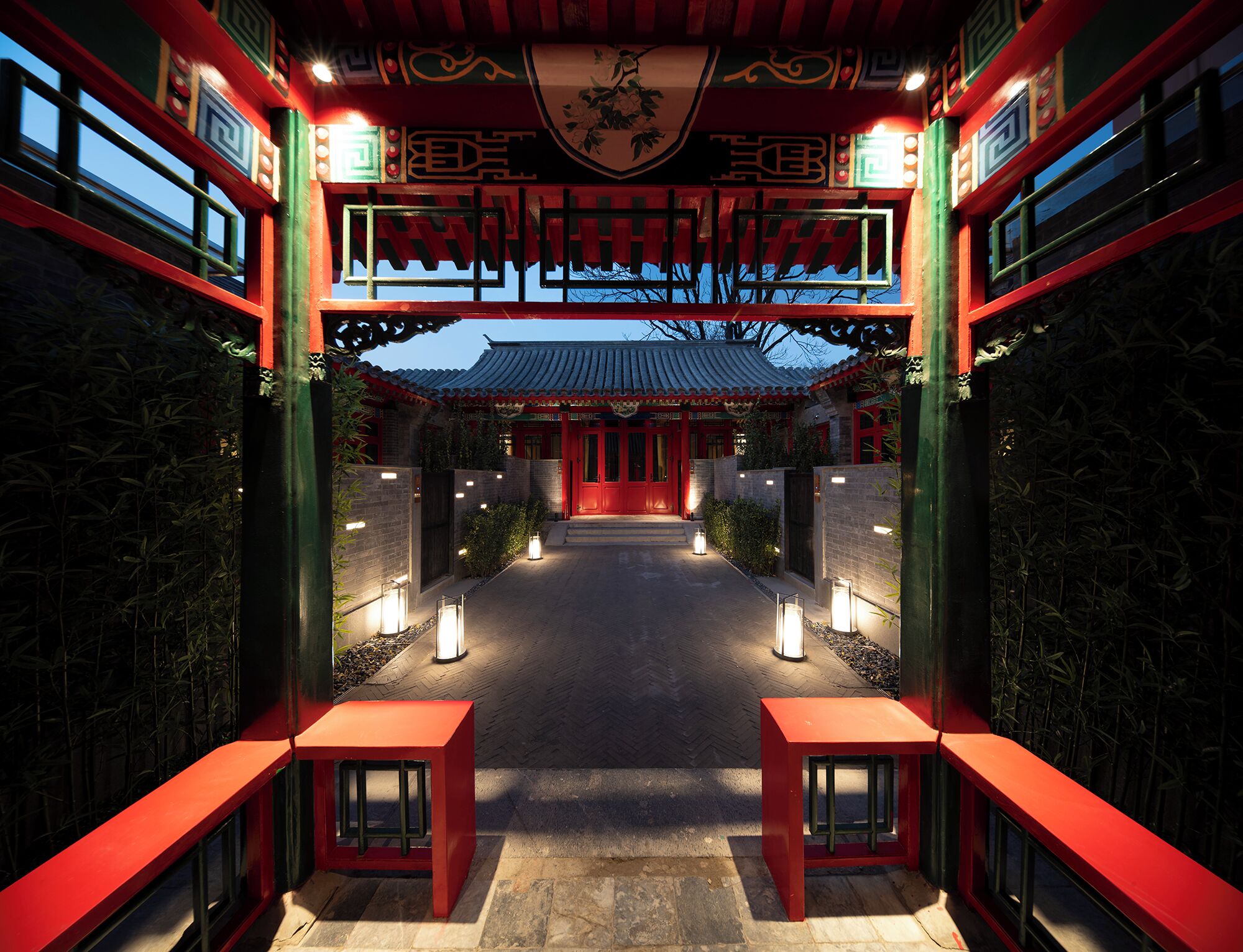 A traditional Chinese gate with red and green colors, leading to a courtyard with lanterns and a tiled floor.