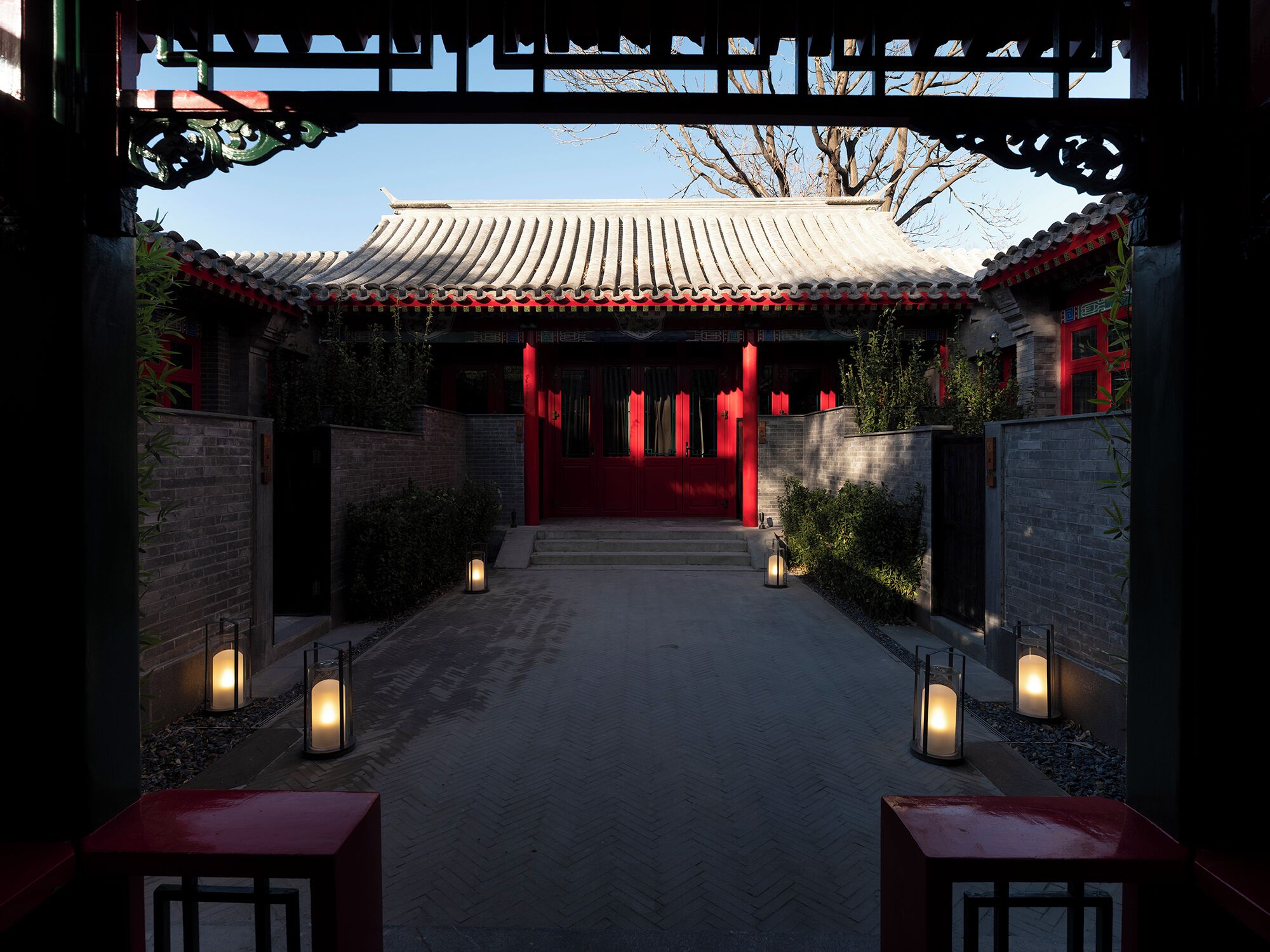 Puerta tradicional china que da a un edificio con techo de tejas y detalles en rojo.