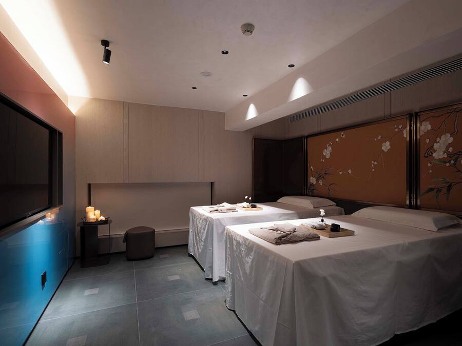 Habitación de hotel con dos camas, un televisor de pantalla plana grande, una mesita con velas y una pared decorada con una pintura floral.