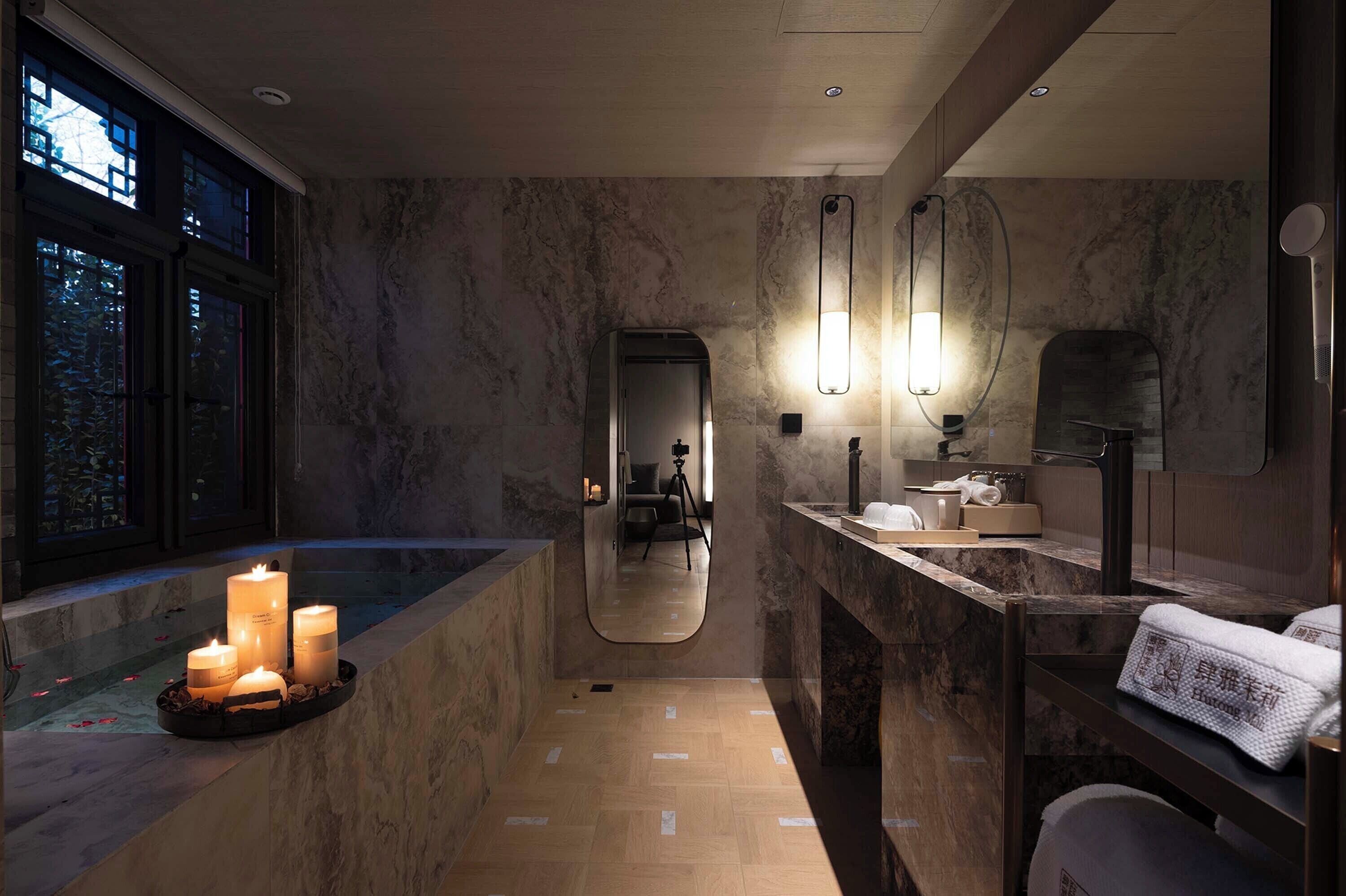 Un bagno moderno con un vanità in marmo, uno specchio grande e candele sul pavimento.