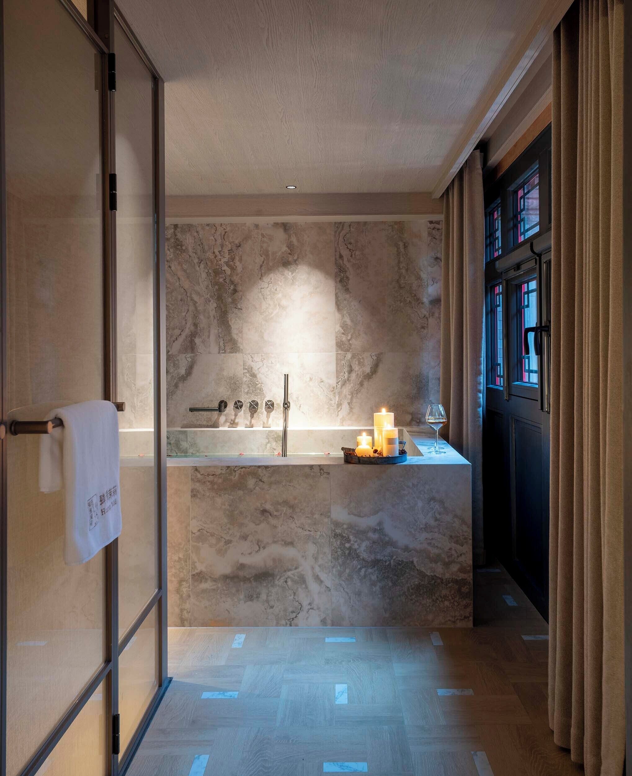 A modern bathroom with a marble vanity, a glass shower enclosure, and a candle-lit ambiance.