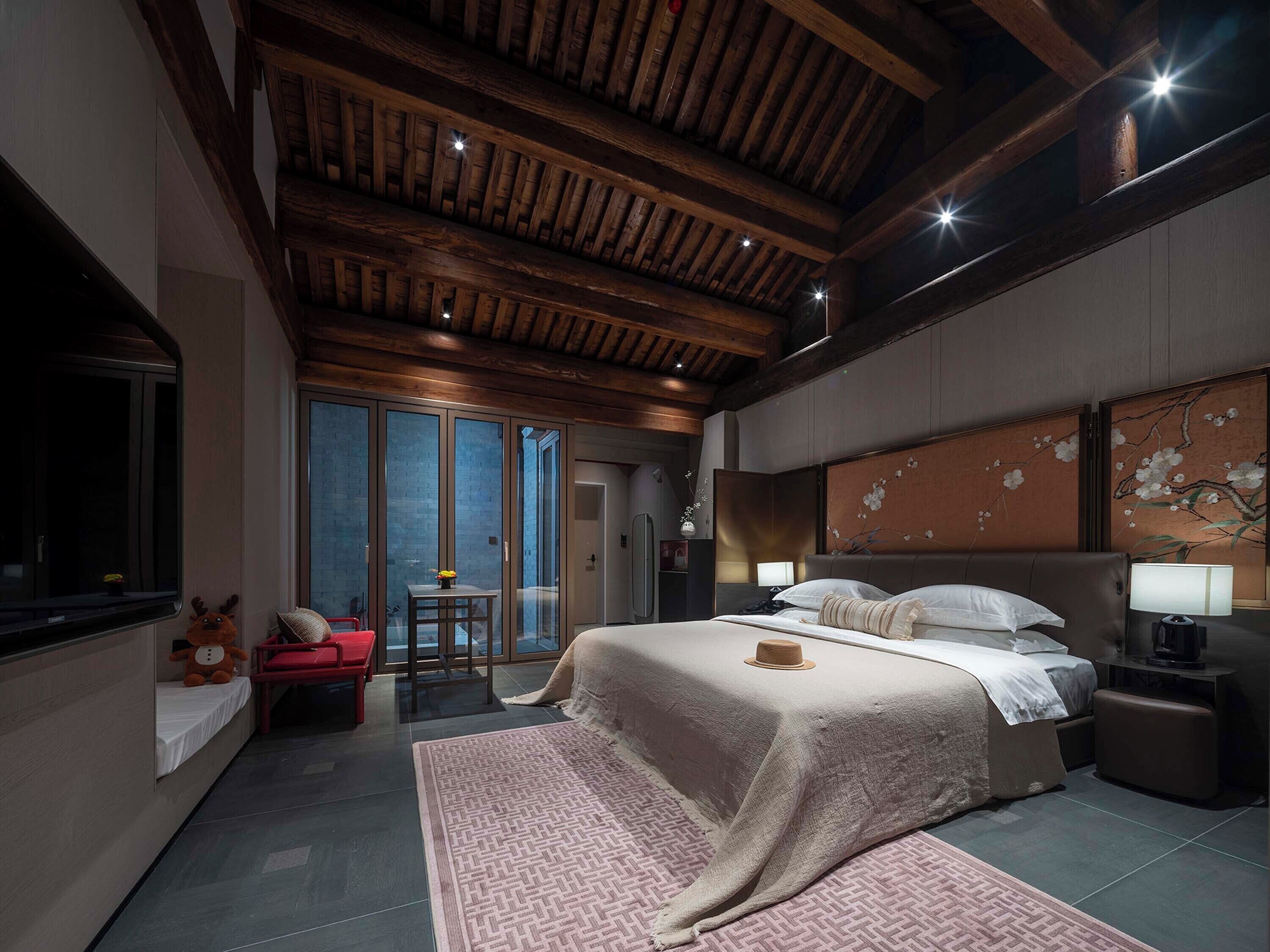Ein modernes Schlafzimmer mit einem großen Bett, einer Holzbalkendecke und Blick durch eine Glastür.