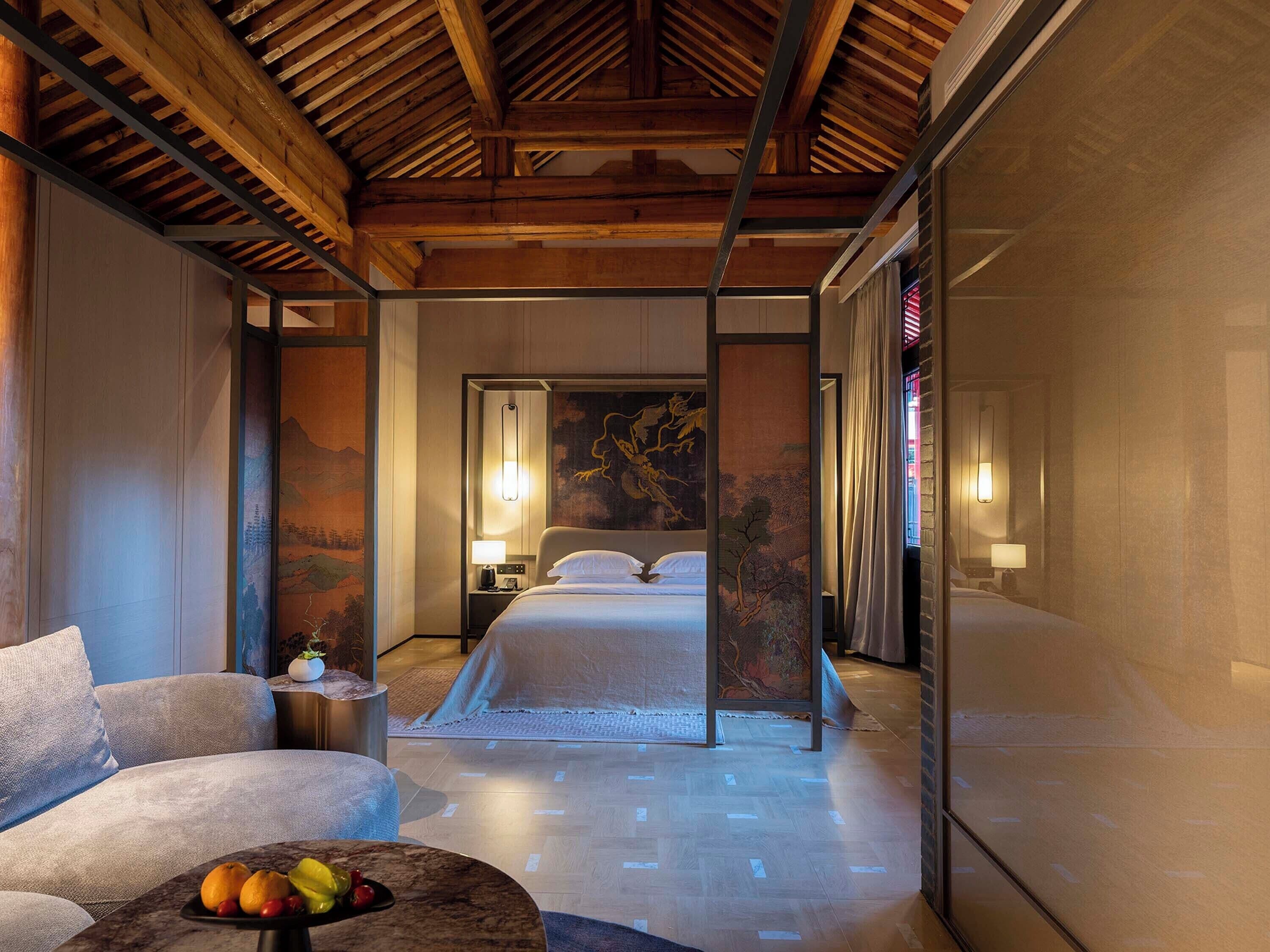 A hotel room with a bed, a sitting area with a table and chairs, and a large painting on the wall.