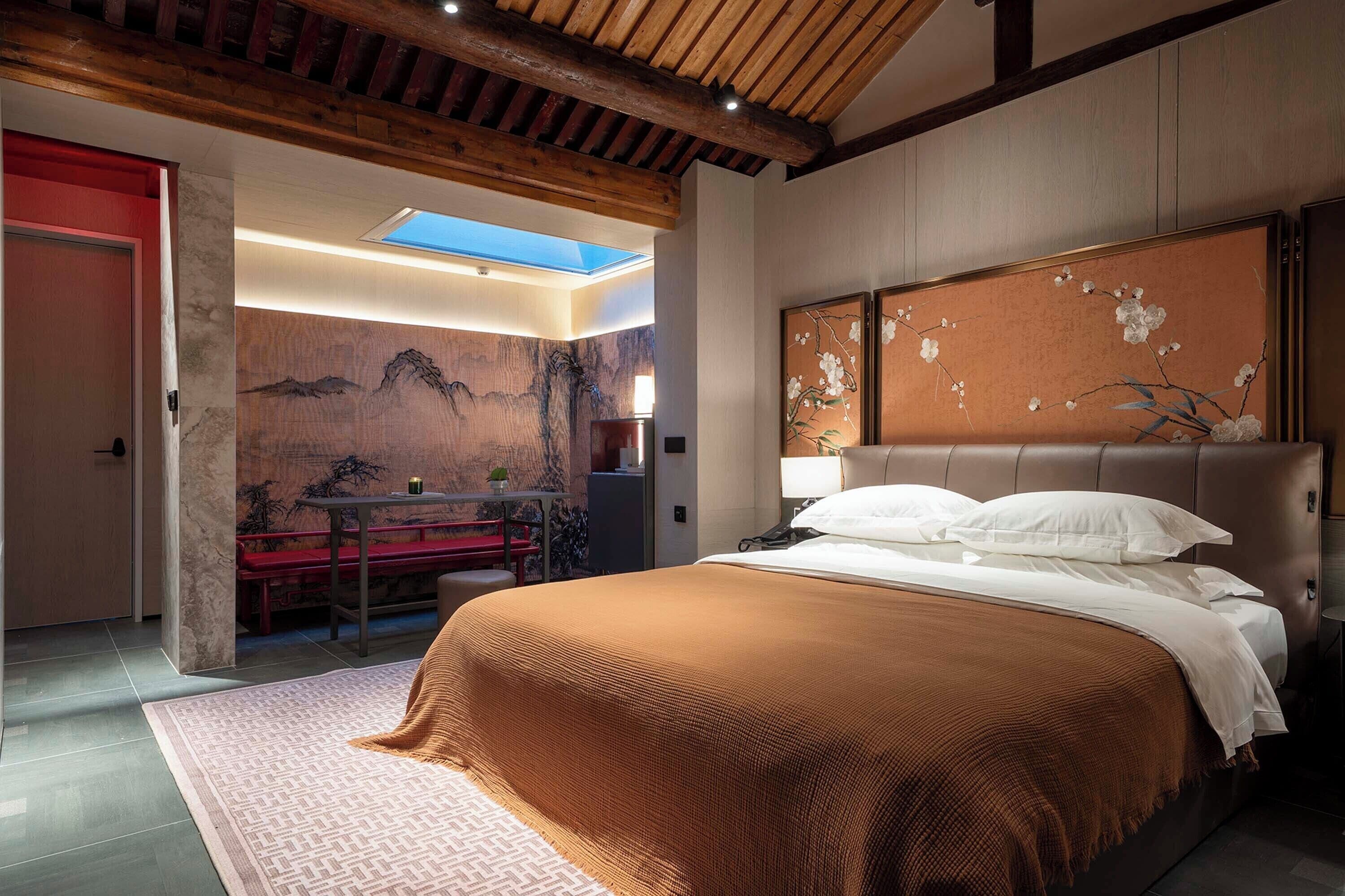 Una camera da letto con un letto grande, una testiera in legno, un lucernario, una panca rossa e un muro con un dipinto floreale.