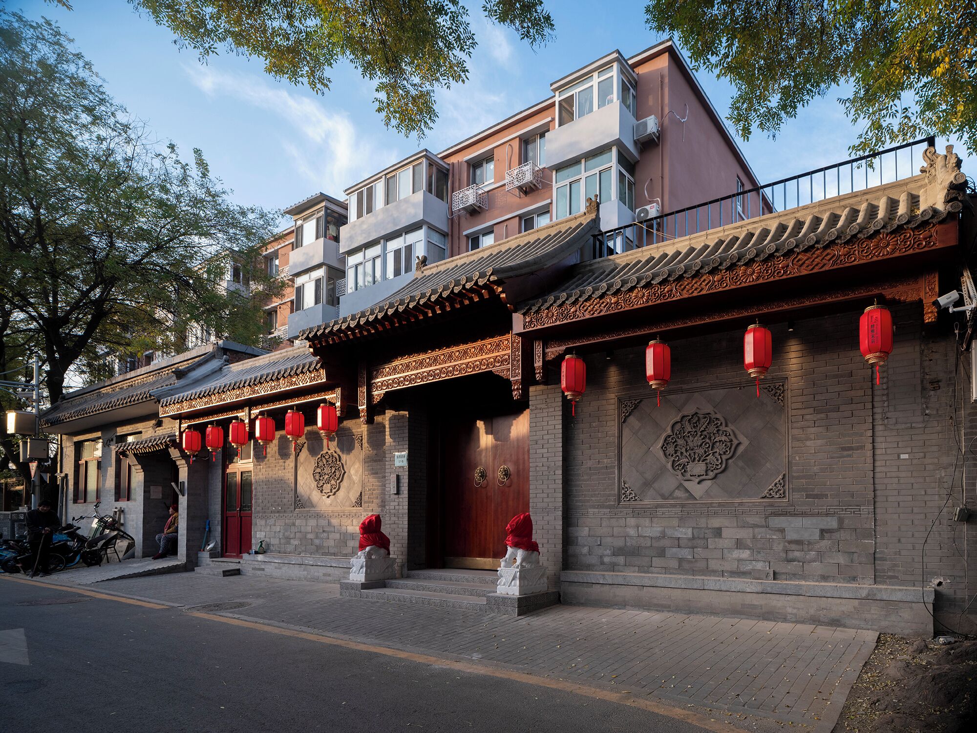 A traditional building with a tiled roof, red lanterns, and a statue in front.