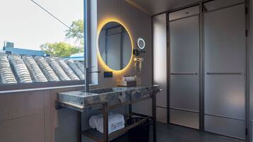 A modern bathroom with a large mirror, a vanity with a marble countertop, a towel rack, and a view of the outside.