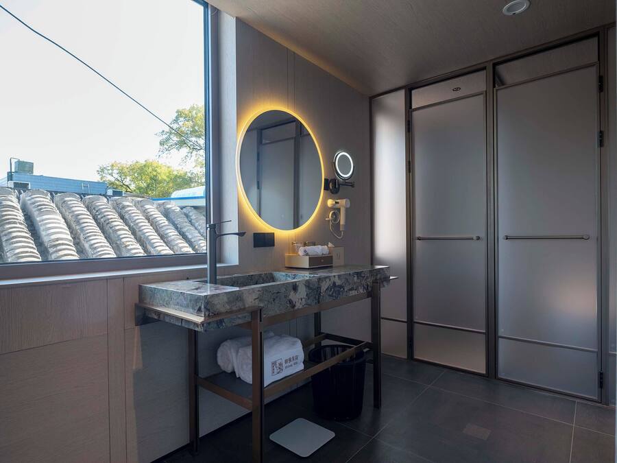 A modern bathroom with a large mirror, a vanity with a marble countertop, a towel rack, and a view of the outside.