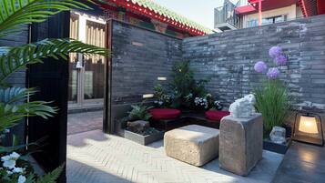 Un patio con techo tradicional, paredes de piedra y una zona de estar con cojines rojos.