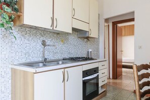 Une cuisine avec des meubles blancs, une cuisinière à gaz et un dosseret carrelé.