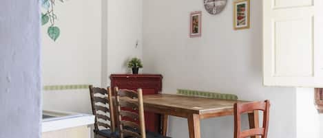 A dining area with a wooden table and chairs, a clock on the wall, and a small plant on the table.