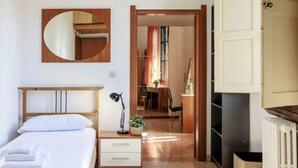 A hotel room with a bed, bedside table, lamp, and a mirror. There is a door leading to a dining area with chairs and a table. - Faenza Huge Apartment (Firenze)