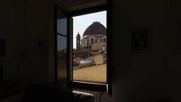 A room with a large window, a radiator, and a view of a building with a dome. - Faenza Huge Apartment (Firenze)